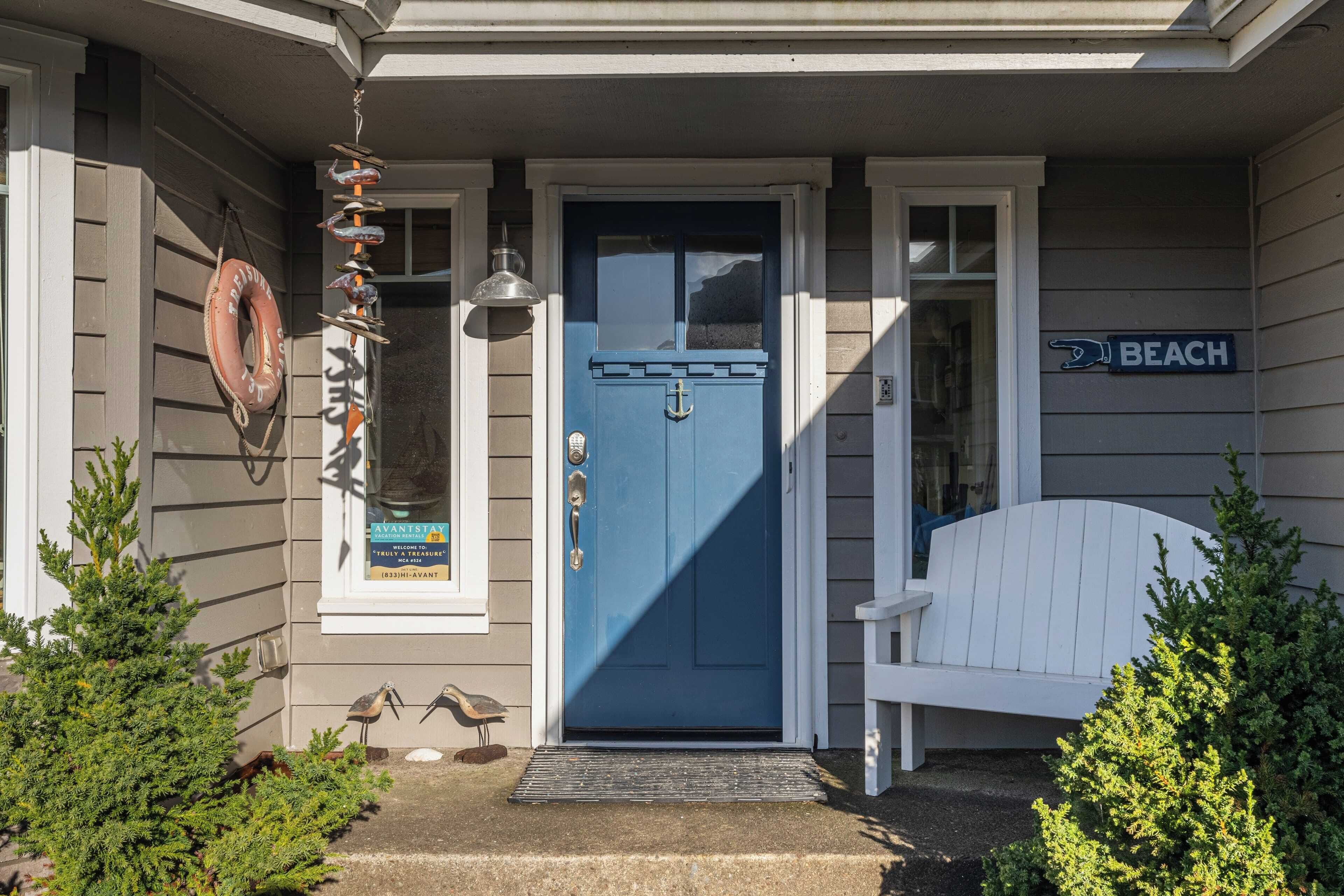 Una casa con puerta azul, un banco blanco y un letrero que dice 'BEACH'.