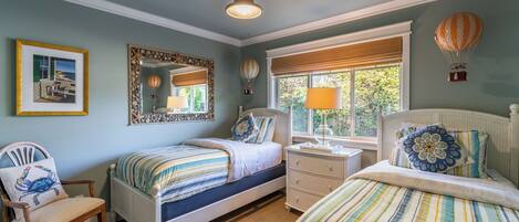 A bedroom with two beds, a window with a view, a mirror with a decorative frame, and a ceiling fan.