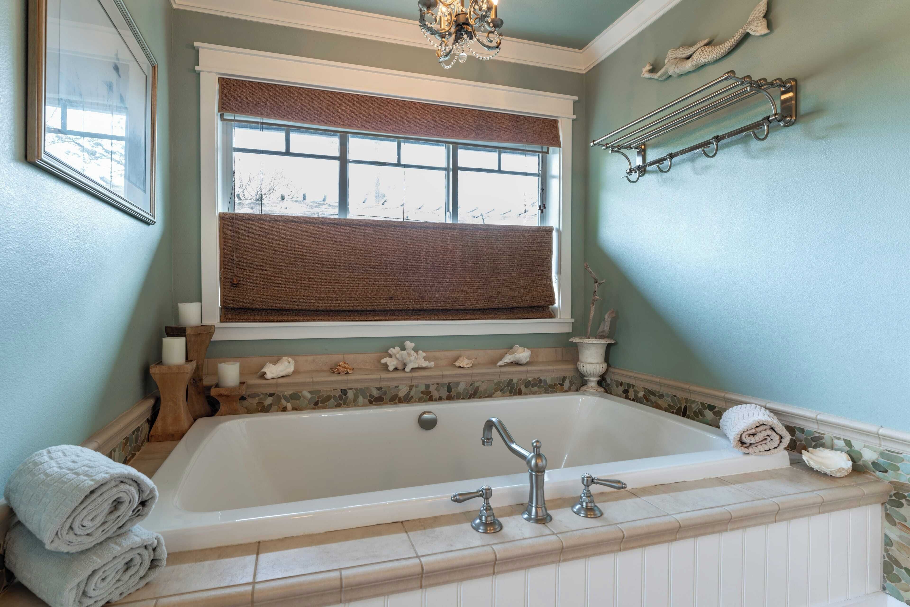 A bathroom with a bathtub, a window with a brown blind, and a decorative towel rack.
