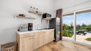 Een moderne keuken met een ingebouwde magnetron, broodrooster en koffiezetapparaat. Er zijn houten keukenkastjes en een roestvrijstalen koelkast. Een raam biedt uitzicht op een zwembad en tuinmeubilair.