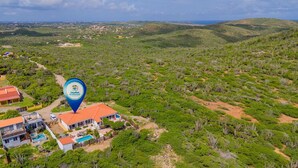 Luchtbeeld van een resort met meerdere gebouwen, een zwembad en een omgeving van groene begroeiing en heuvels.