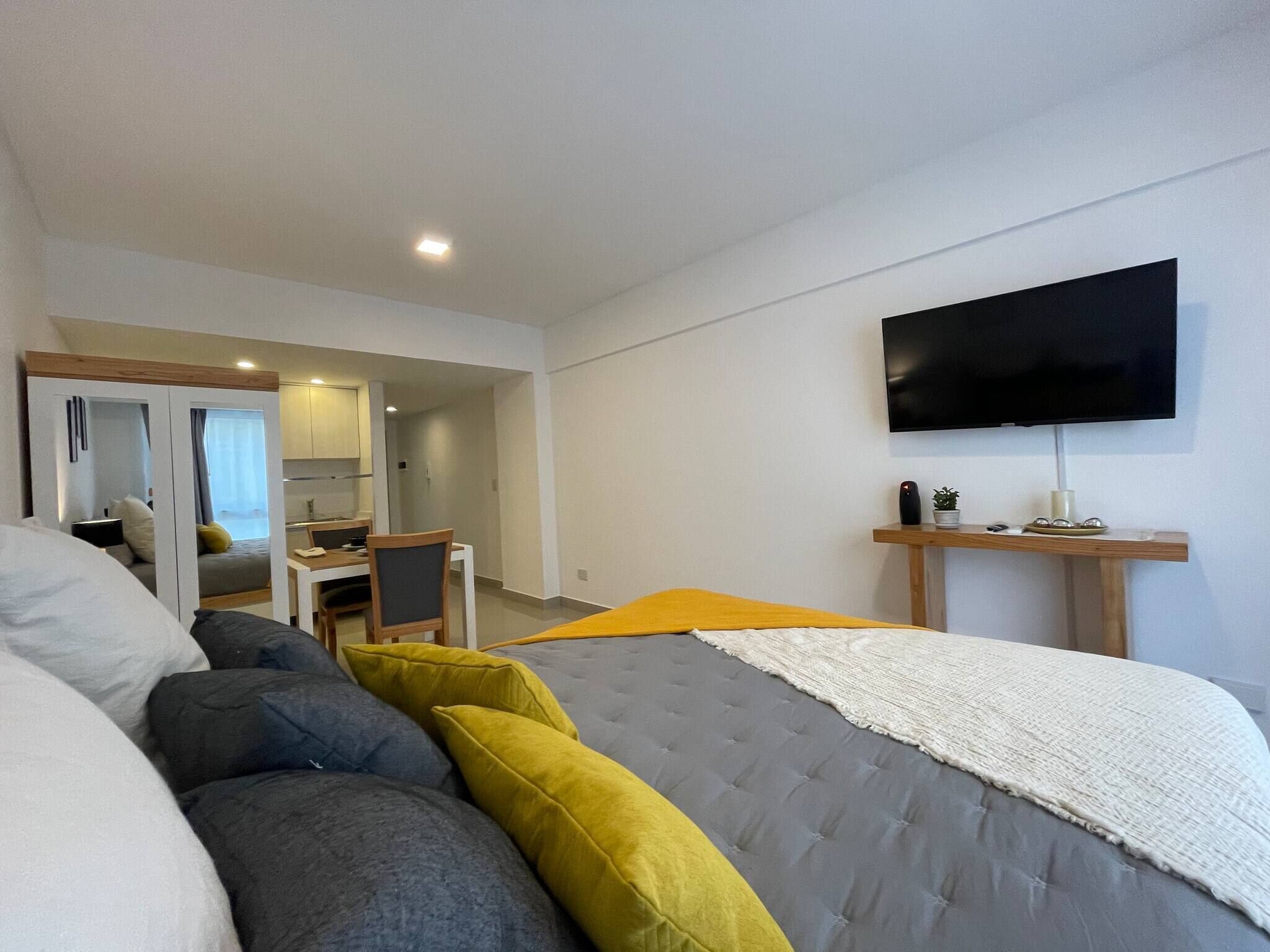 A modern bedroom with a bed, a desk, a chair, a TV, and a mirror.