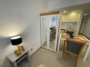 A modern kitchen with white cabinets, a dining area with a wooden table and chairs, and a small side table with a lamp.
