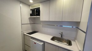 A compact kitchen with white cabinetry, a built-in microwave, a stainless steel sink, and a dishwasher. - Modern & Cozy Studio in San Telmo No7155 (Buenos Aires)