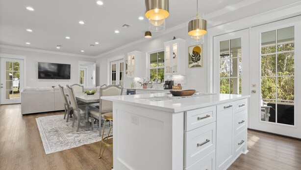 A spacious kitchen with white cabinetry, a large island, pendant lighting, and a view of the outdoors. - Yeah, Bay-by! Modern Farmhouse in Old Town Bay Saint Louis (Bay St. Louis)