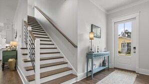 A staircase with wooden steps and white railings, a light blue console table with decorative items, and a white rug on a wooden floor. - Yeah, Bay-by! Modern Farmhouse in Old Town Bay Saint Louis (Bay St. Louis)