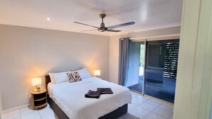 A bedroom with a bed, bedside lamps, a ceiling fan, and a view of the outdoors.