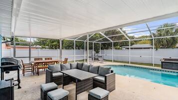 Eine überdachte Terrasse im Freien mit Pool, Korbmöbeln und Grill.
