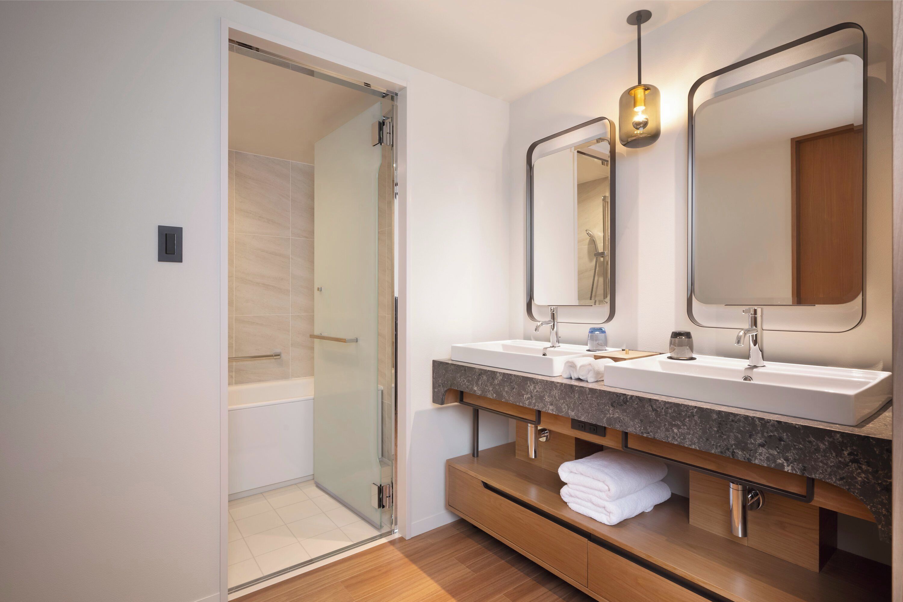 A modern bathroom with a glass shower door, two sinks, a vanity with a mirror, and a towel rack.