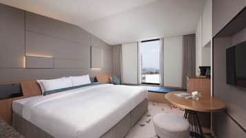 A modern hotel room with a large bed, a small round table, a seating area, and a television.