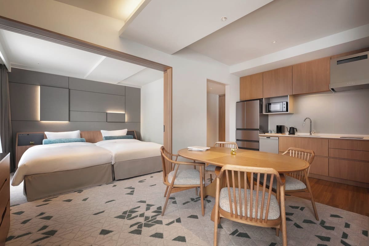 Ein modernes Hotelzimmer mit einem großen Bett, einem Esstisch mit Stühlen, einer Küchenzeile und einem separaten Badezimmer.