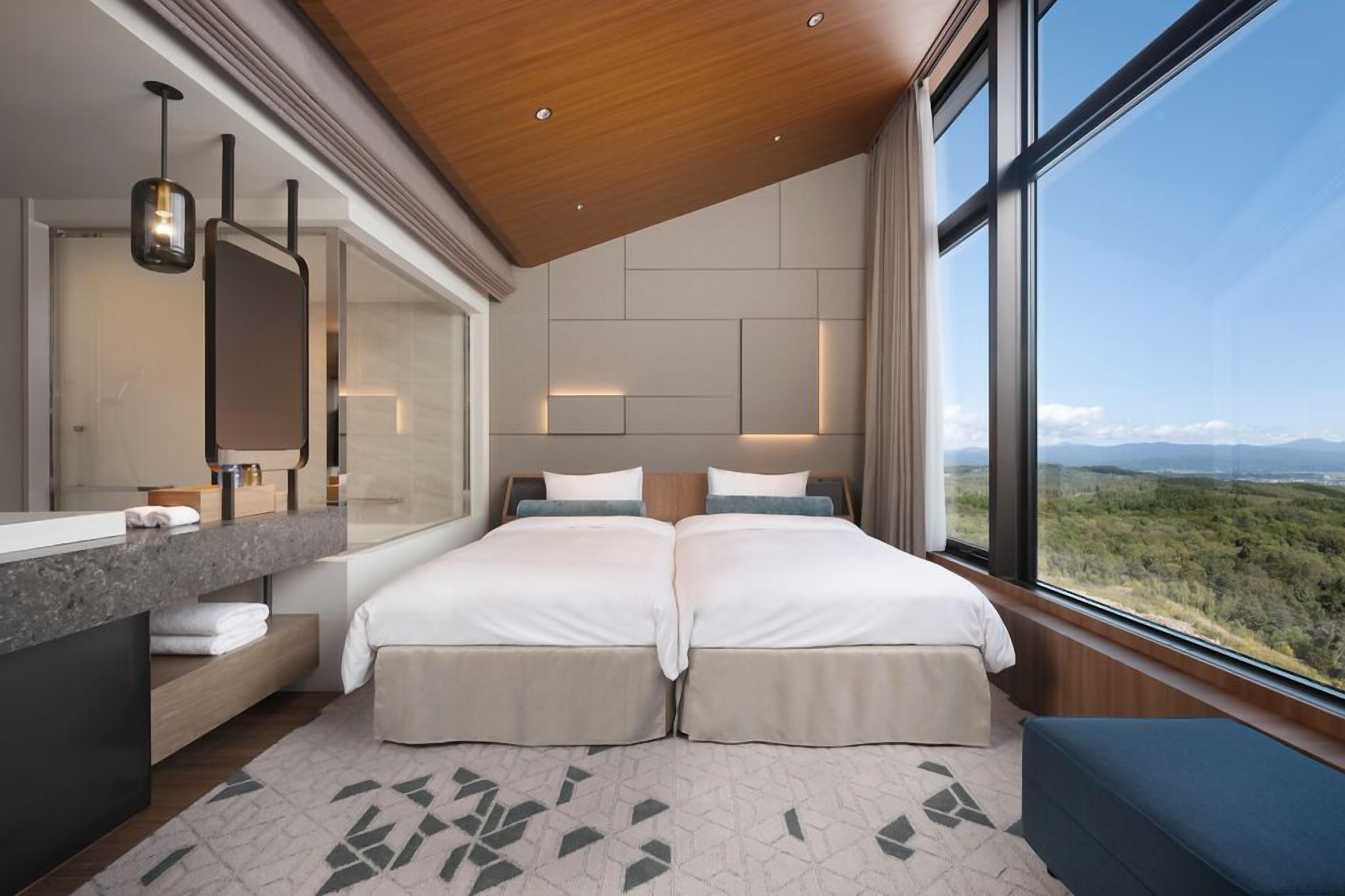 A modern hotel room with a large bed, a bathroom with a vanity, and a view of the landscape.