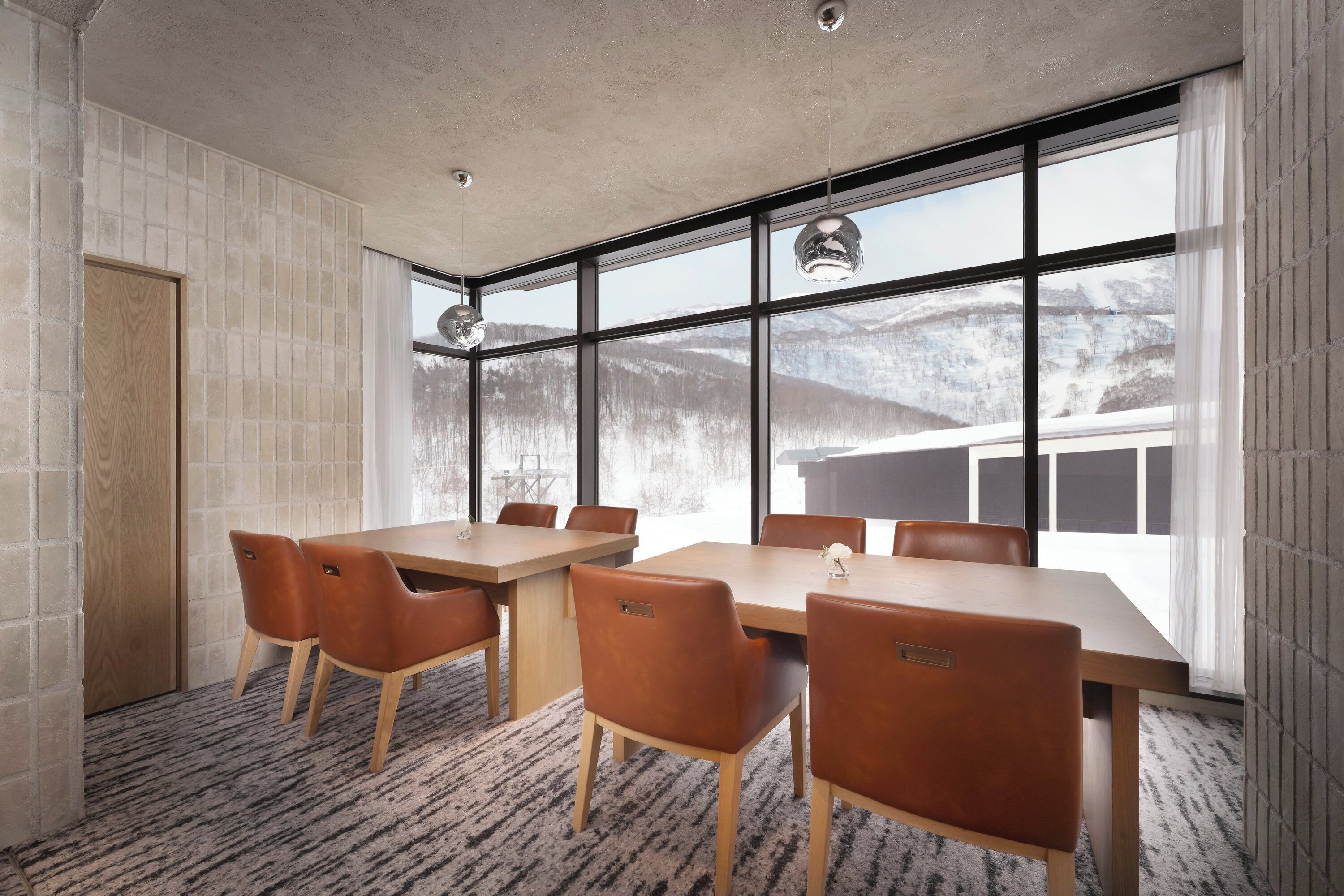 A conference room with a large table and chairs, large windows with a view of mountains, and a textured carpet.