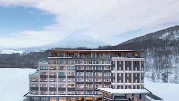 A modern hotel with multiple floors, large windows, and a snowy landscape with a mountain in the background.