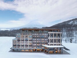 Un hôtel moderne à plusieurs étages, doté de grandes fenêtres et offrant une vue sur un paysage enneigé avec une montagne en arrière-plan.