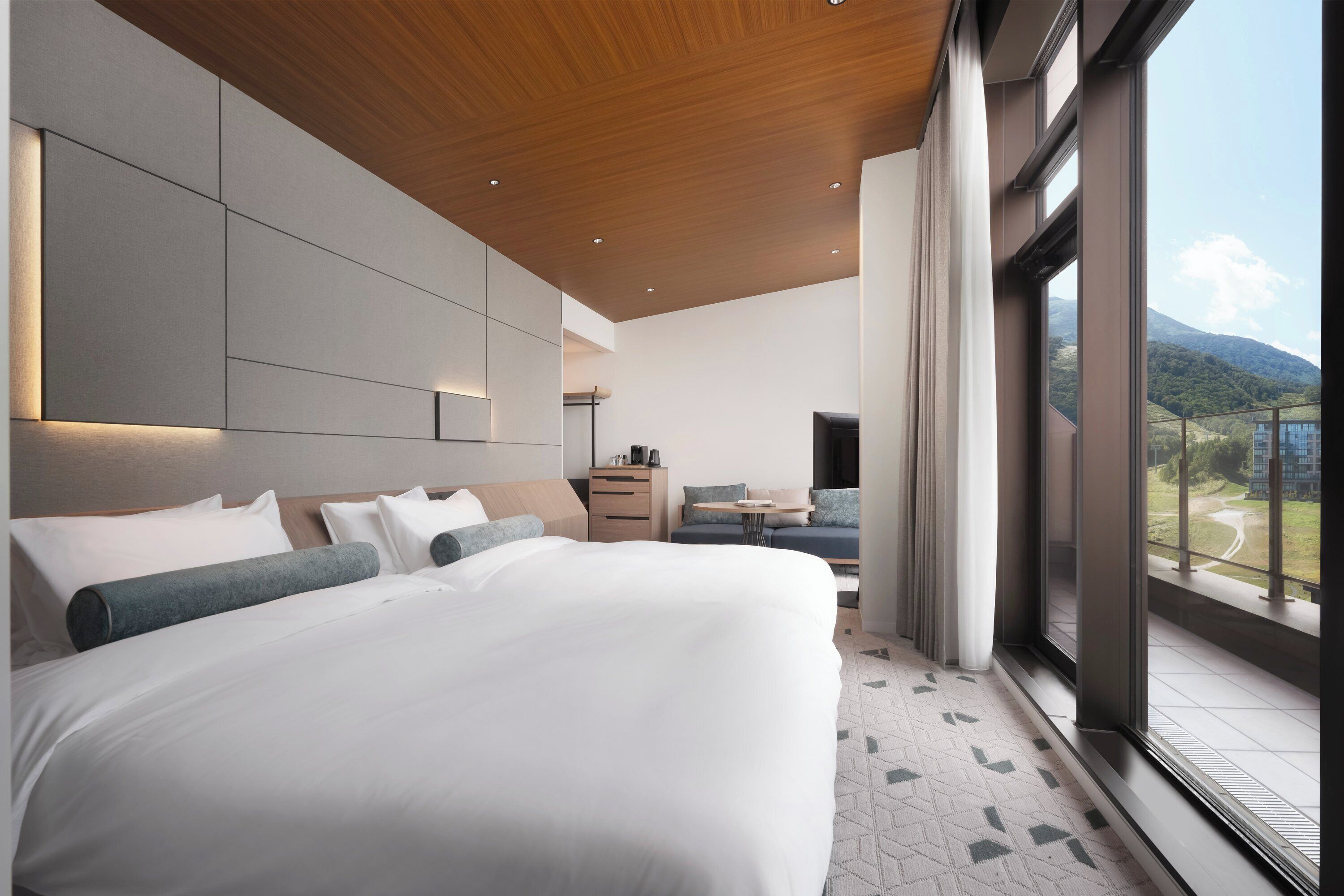 A modern hotel room with a large bed, a desk, and a view of the mountains.