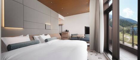 A modern hotel room with a large bed, a desk, and a view of the mountains.