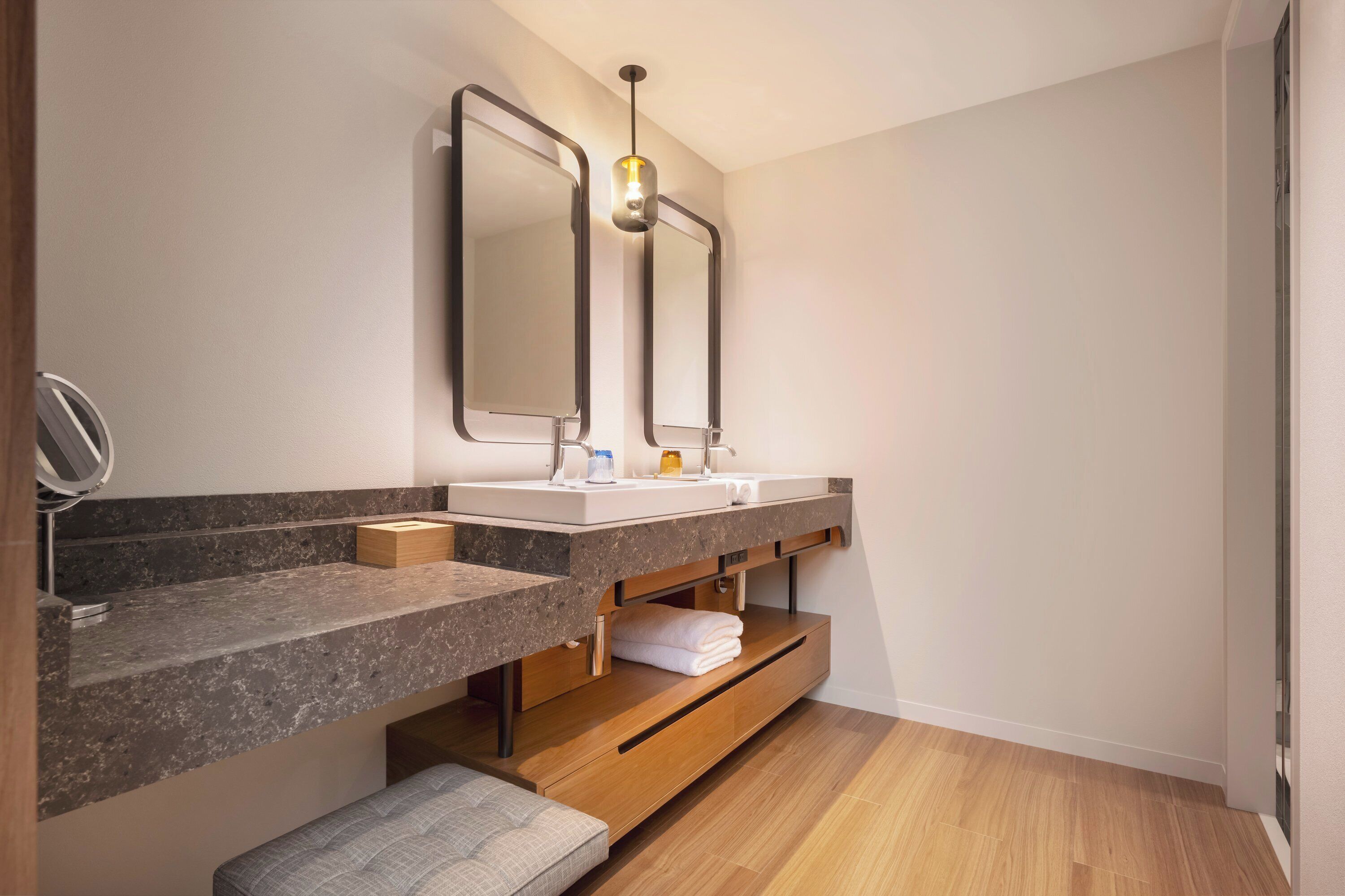 A modern bathroom with two sinks, a vanity with a mirror, a towel rack, and a wooden bench.