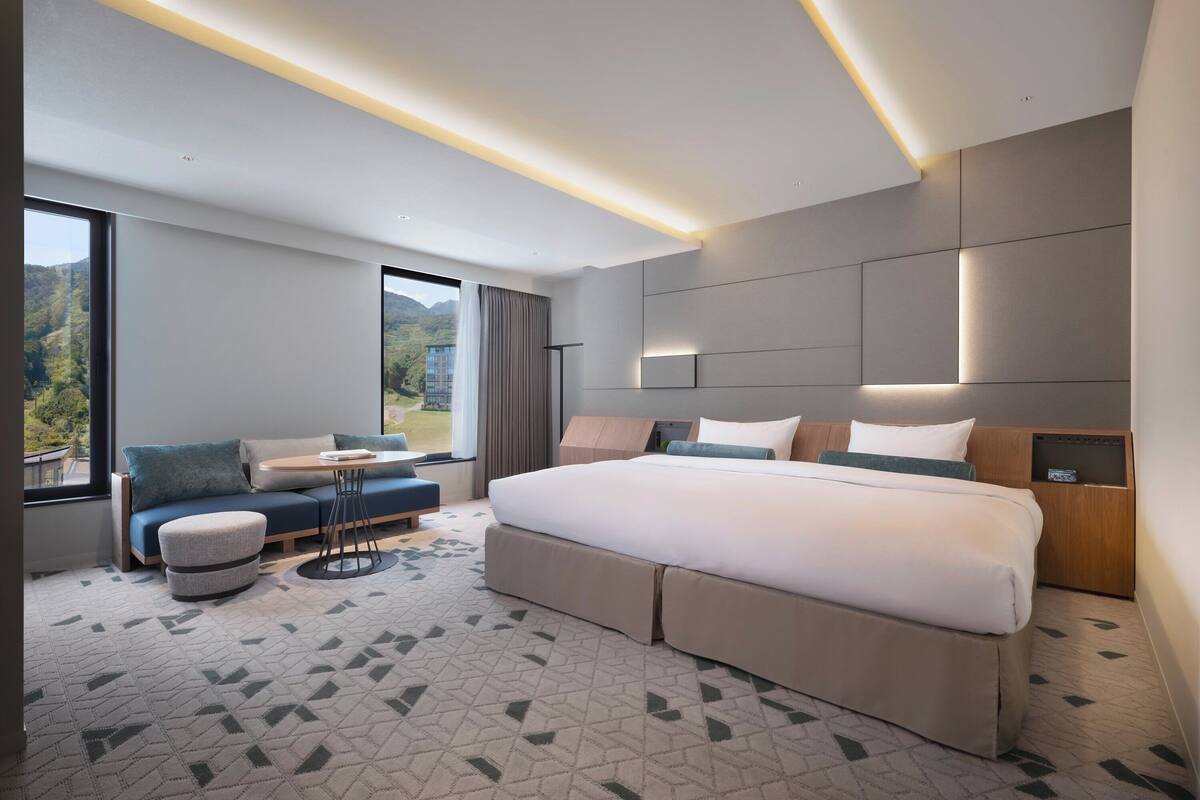 Ein modernes Hotelzimmer mit einem großen Bett, einer Sitzecke, einem kleinen Tisch und Blick ins Freie.