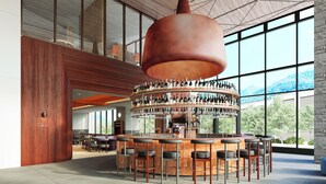 Un área de bar moderna con barra circular, varios taburetes y una lámpara colgante grande.
