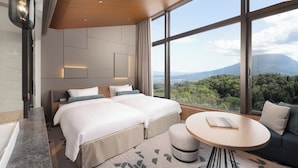 Una habitación de hotel moderna con dos camas, una mesa redonda y un gran ventanal con vistas a la montaña.