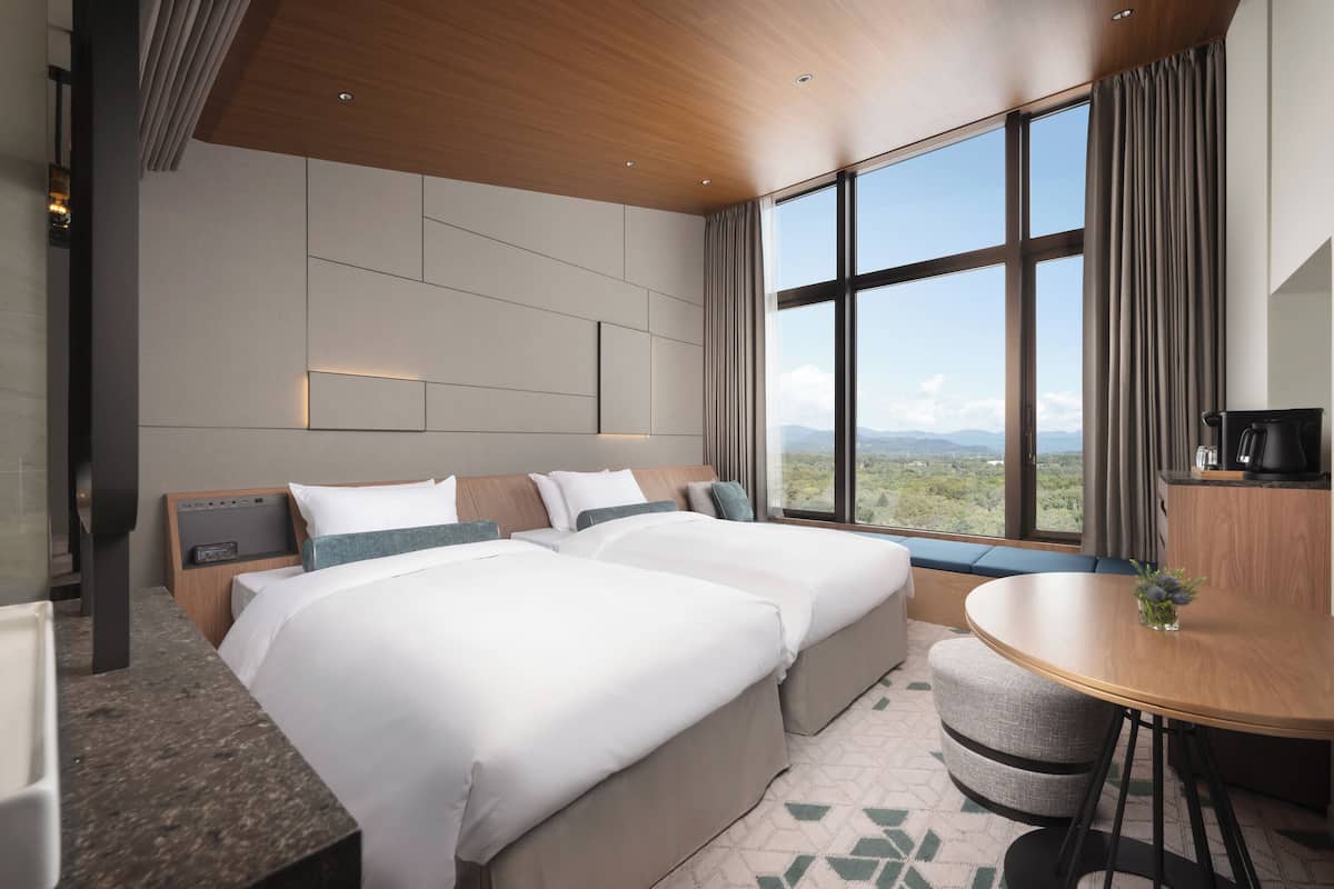 Ein Hotelzimmer mit zwei Betten, einem kleinen runden Tisch, Bergblick und modernem Design.