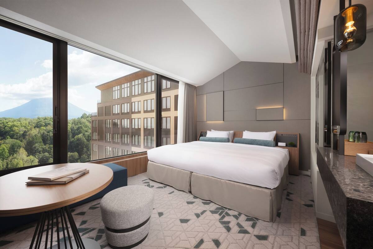 Ein modernes Hotelzimmer mit einem großen Bett, einem runden Tisch und Blick auf Stadt und Berge.