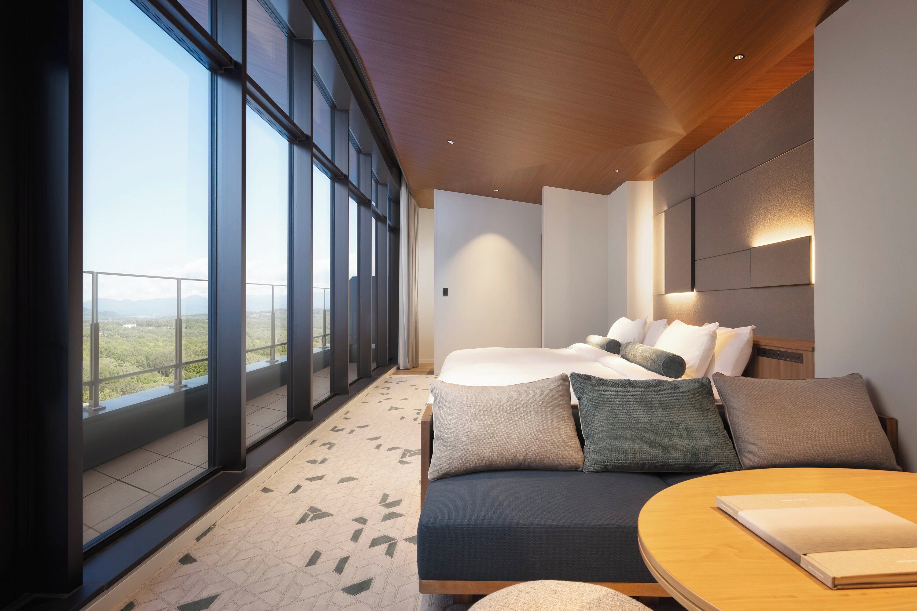 Une chambre d’hôtel moderne, dotée d’un grand lit, d’un canapé et offrant une vue sur le paysage grâce à de grandes fenêtres.