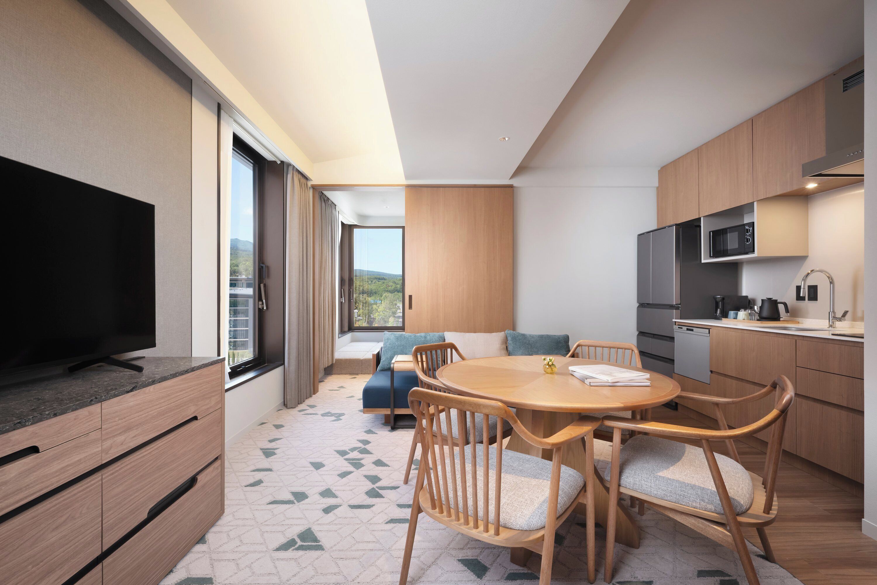 A modern kitchen with a dining area, a flat-screen TV, and a view of the outdoors.