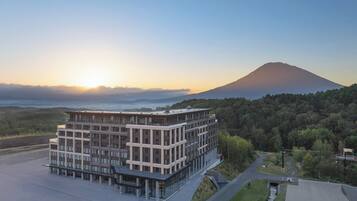 Un edificio moderno de varios pisos con techo plano, rodeado de un área ajardinada con un sendero que lo conduce.