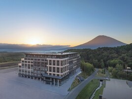 Un edificio moderno de varios pisos con techo plano, rodeado de un área ajardinada con un sendero que lo conduce.