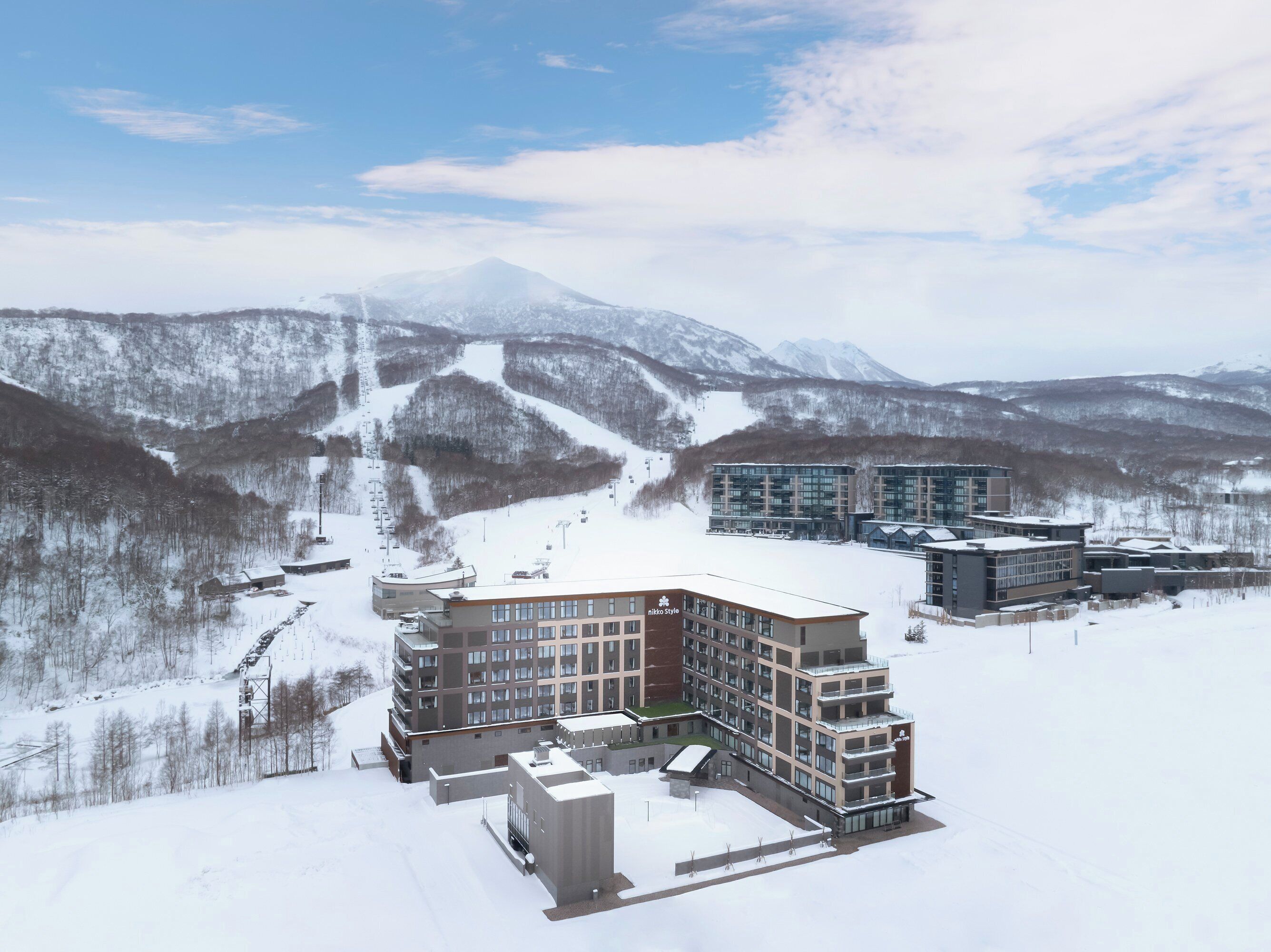 A modern hotel complex with multiple buildings, surrounded by snow-covered mountains and a ski slope.
