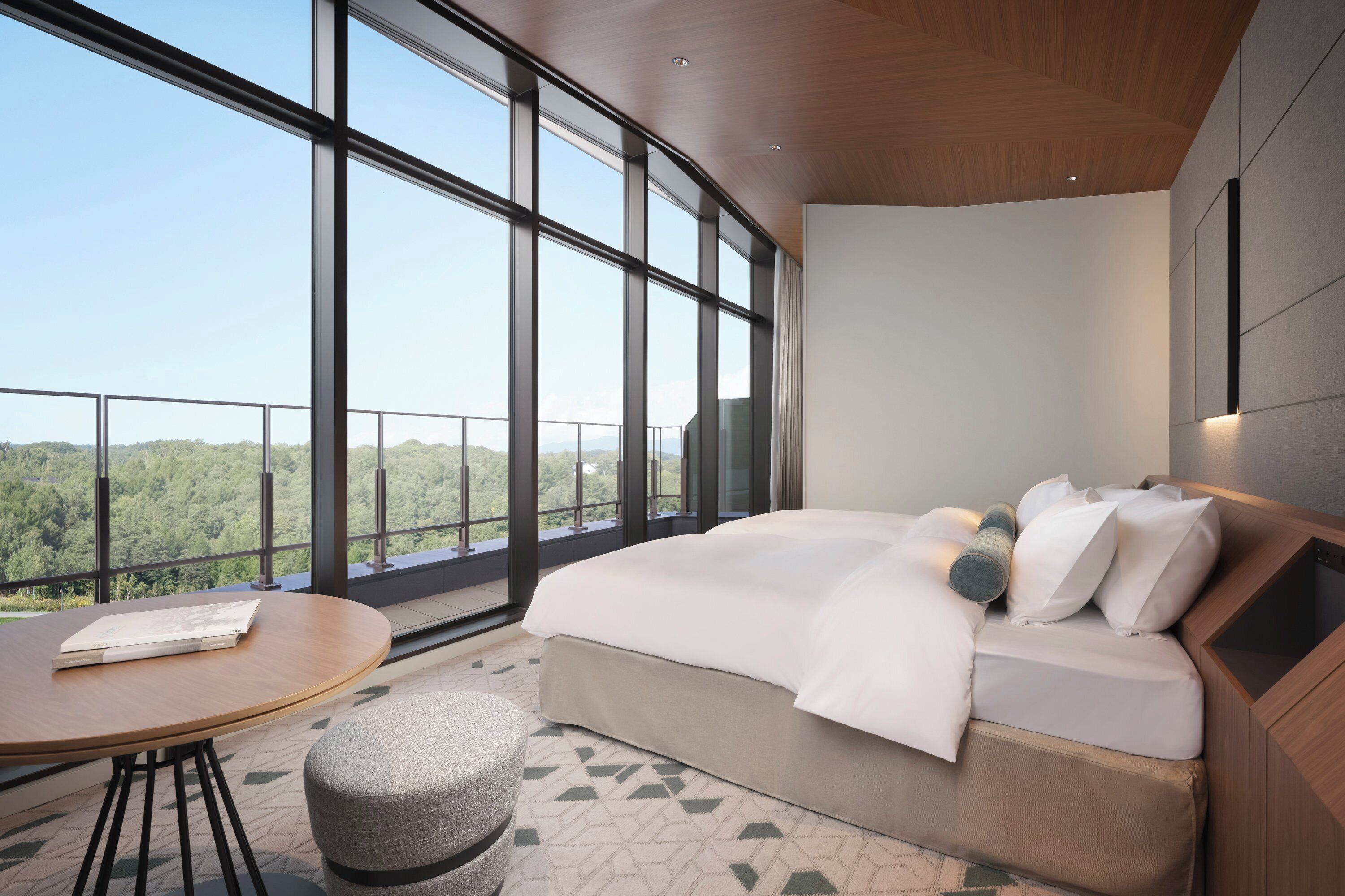 A modern hotel room with a large bed, a round table, and a view of the forest.