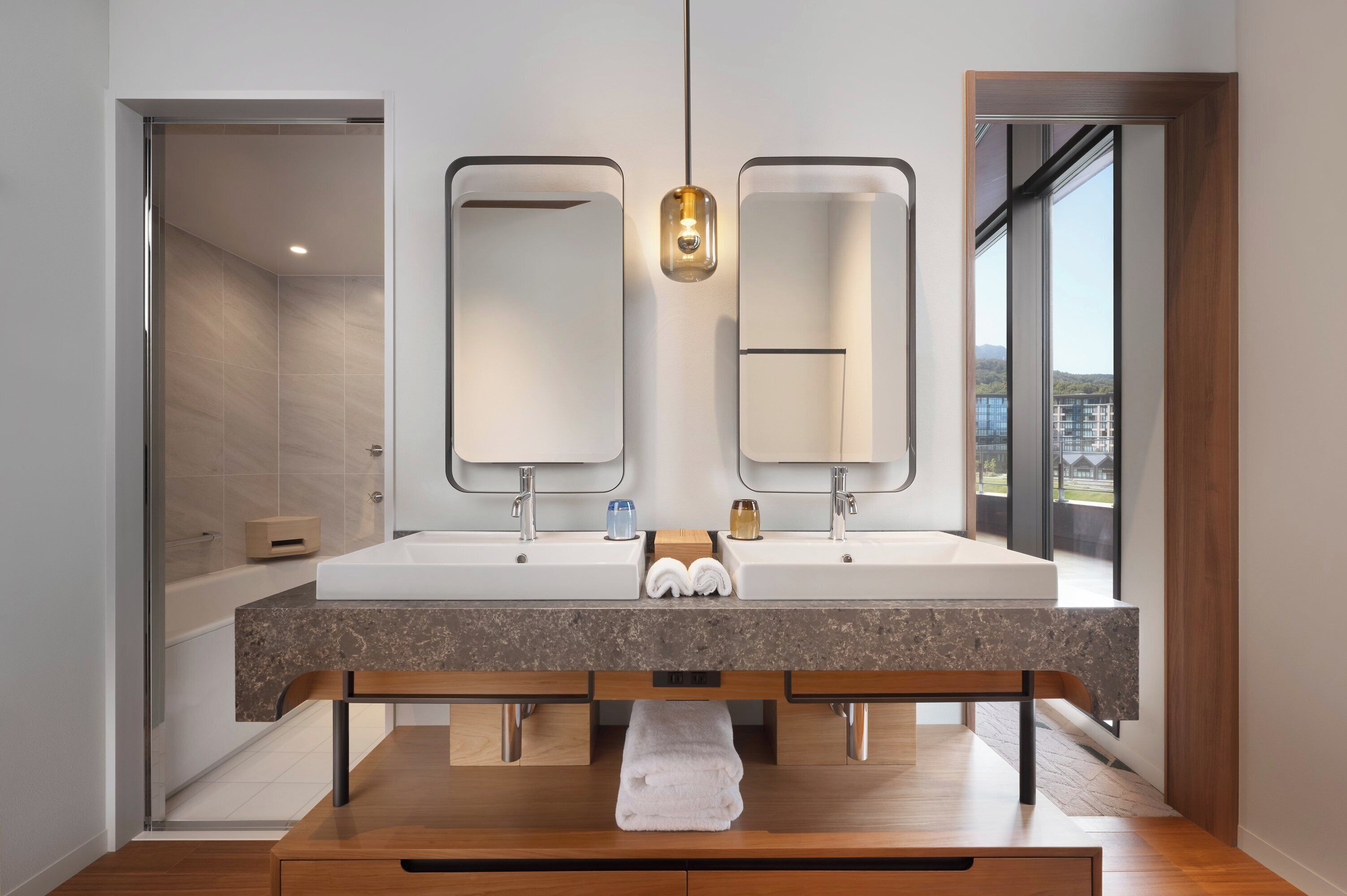 Un baño moderno con lavamanos doble, un espejo grande y un banco con toallas.