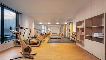 A modern gym with exercise equipment, wooden flooring, and large windows.