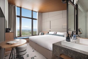Une chambre d’hôtel moderne avec un grand lit, une table ronde, une salle de bain dotée d’un grand miroir et une vue sur le paysage grâce à de grandes fenêtres.