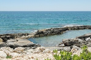 Una costa rocciosa con mare cristallino e orizzonte lontano.
