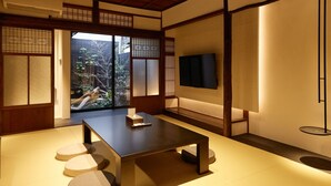 A traditional Japanese room with tatami flooring, a low table with cushions, sliding doors, and a TV mounted on the wall. - Tsumugi Kamiurokogatacho (Kyoto)