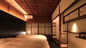 A traditional Japanese-style bedroom with a large bed, wooden ceiling beams, and sliding doors. - Tsumugi Kamiurokogatacho (Kyoto)