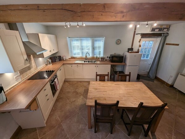 A kitchen with a wooden table, white cabinets, and a window with blinds.