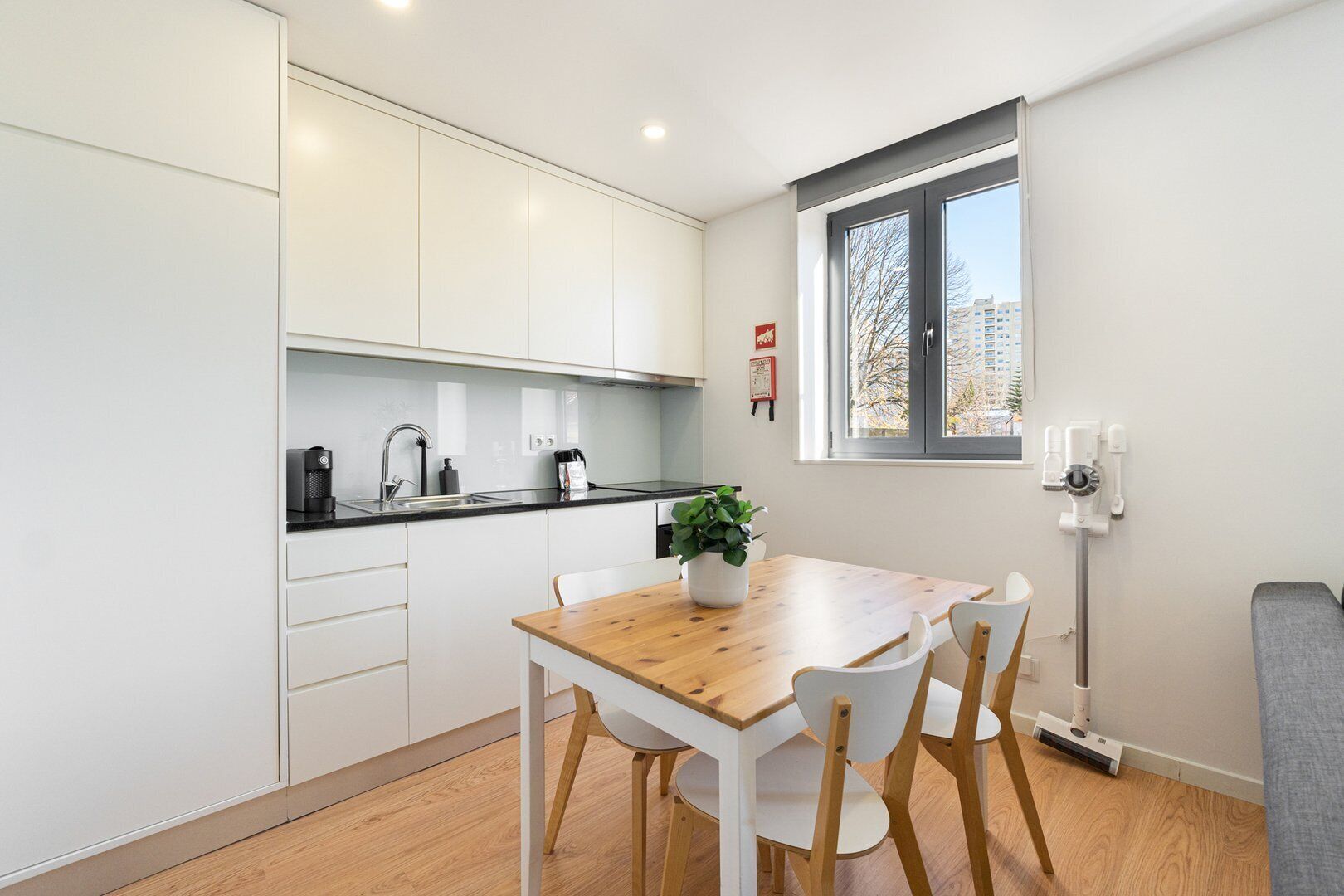 A modern kitchen with white cabinets, a wooden dining table, and a window with a view of buildings.
