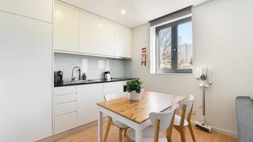 A modern kitchen with white cabinets, a wooden dining table, and a window with a view of buildings.