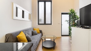 A modern living room with a grey sofa, yellow cushions, a glass coffee table, a flat-screen TV, and a potted plant. - GuestReady - King's Retreat (Porto)
