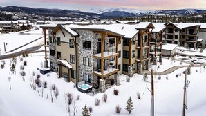 A multi-story hotel with a stone facade, balconies, and a view of snow-covered mountains. - Elk Creek D102 private hot tub - 4 beds, sleeps 7 (Fraser)