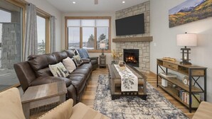 A living room with a fireplace, leather sofa, wooden coffee table, and a television mounted on the wall. - Elk Creek D102 private hot tub - 4 beds, sleeps 7 (Fraser)
