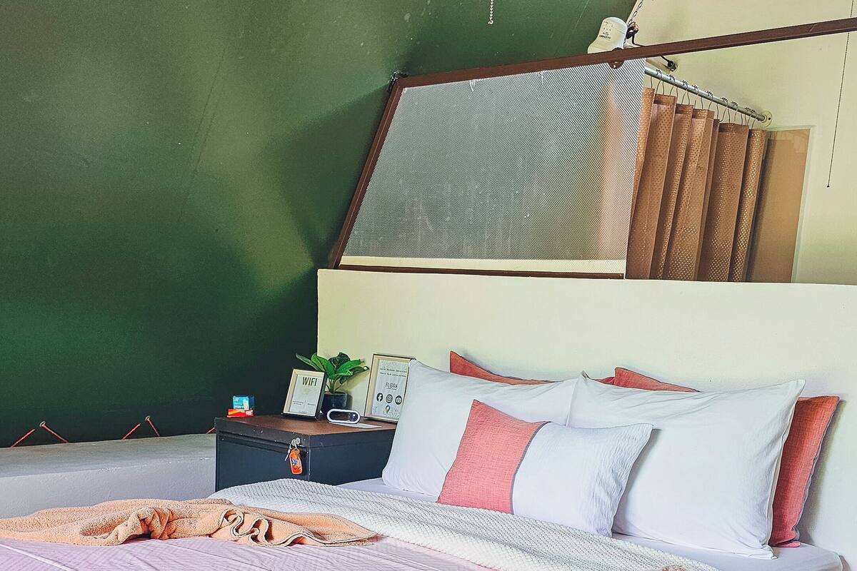 Een slaapkamer met een bed, een nachtkastje, een wandplank en een raam met gordijnen.