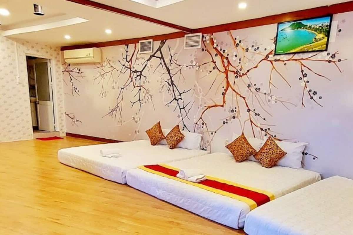 Ein Hotelzimmer mit Holzboden, zwei Betten mit weißer Bettwäsche und dekorativen Kissen, einem Holzschrank und einem Wandbild mit Ästen und Blättern.