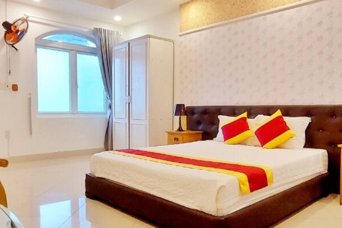 Ein Hotelzimmer mit einem großen Bett, Nachttischen, einem Sessel, einem Schreibtisch und einem fenster mit Vorhängen.