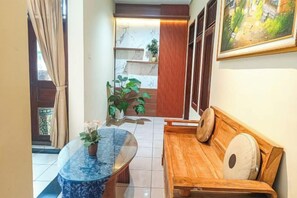 A hallway with a wooden bench, a round table with a plant, and a painting on the wall. - Miraa Guest House & Resto (Denpasar)