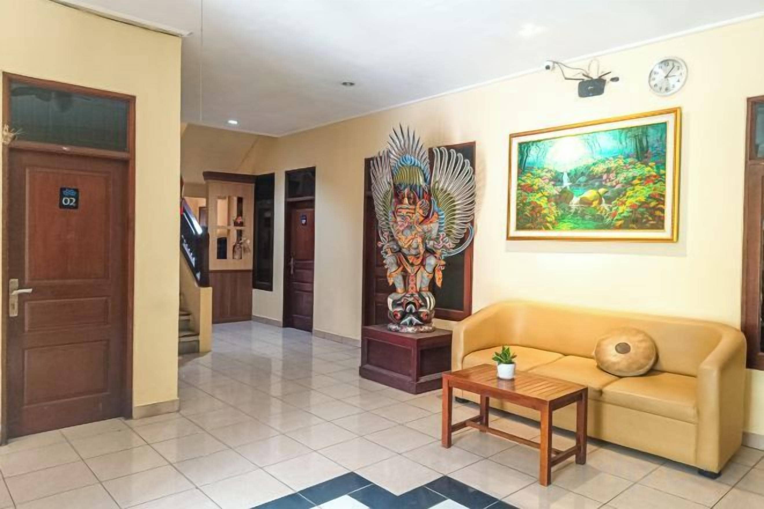A hotel lobby with a reception desk, a sofa, a decorative statue, and a painting on the wall.